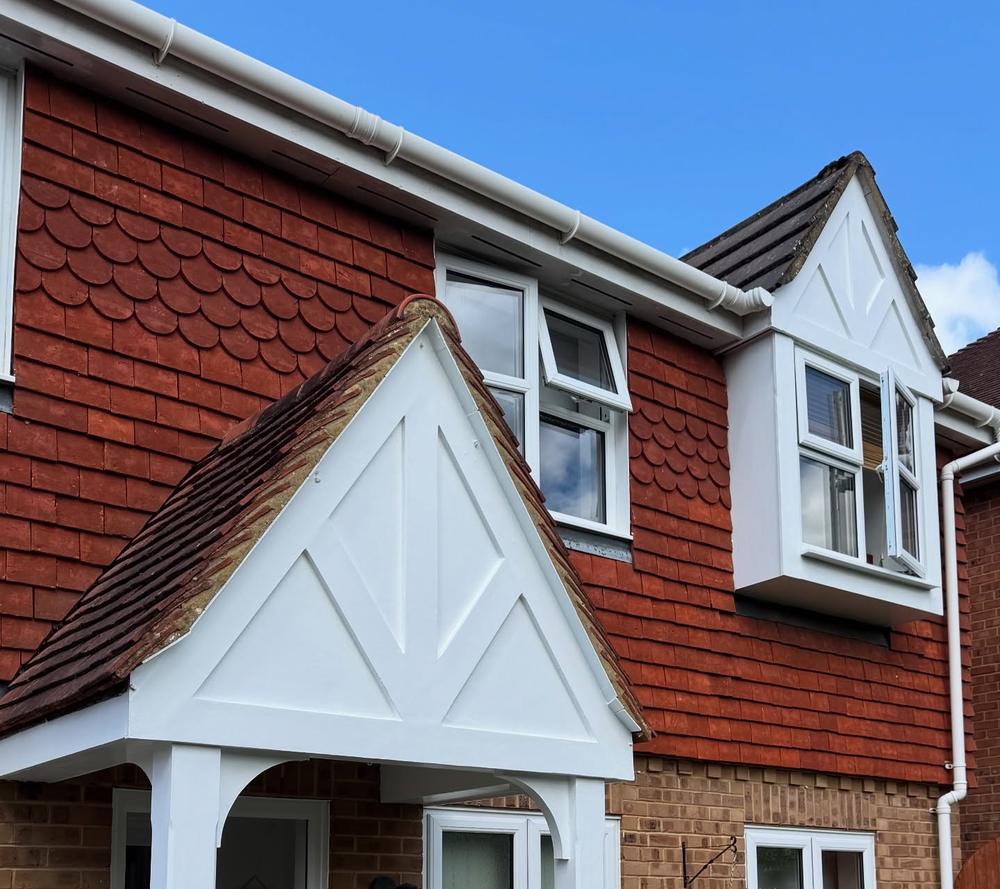 Freshly painted white porch gable and dormer against red tile-hung walls and blue sky